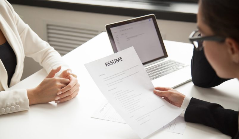 Company CEO and HR manager reading applicant resume or cv while employee waiting for questions, discussion and result during recruitment process in office. Concept of hiring, employment. Close up view